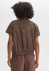 Brown short-sleeve shirt with black vertical stripes, featuring an elastic hem and a simple collar. Smooth fabric texture, relaxed design.