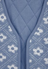 Blå vadderad tyg med ett blommönster. Designen har en slät textur med en kontrasterande solid blå kant runt halsringningen.