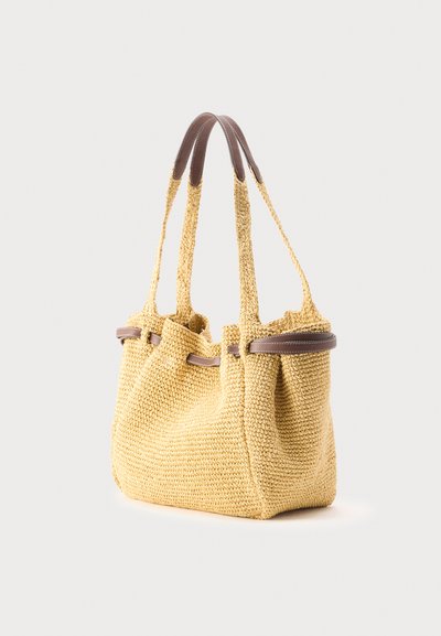 Υφαντή μπεζ τσάντα ώμου με δύο μακριές λαβές με καφέ δερμάτινες λεπτομέρειες στα πάνω μέρη και στις πλευρές των λαβών.