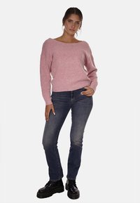 Maglione rosa a maglia strutturata con scollo ampio, abbinato a jeans slim-fit blu scuro e stivaletti neri con lacci.