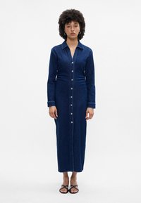 Σκούρο μπλε τζιν φόρεμα με μακριά μανίκια, κουμπιά μπροστά, γιακά και ίσια γραμμή. Μαλακή υφή και ελάχιστες ραφές.