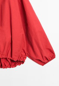 Veste-pull rouge avec des manches larges, un ourlet élastique froncé et un tissu doux et léger. Texture lisse avec un minimum de détails.