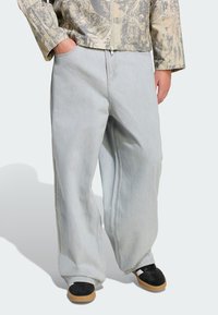 Svetlošedé široké rifle majú mäkk�ú denimovú textúru, detailné šitie a bočné vrecká, doplnené čiernou obuvou a vzorovanou bundou.