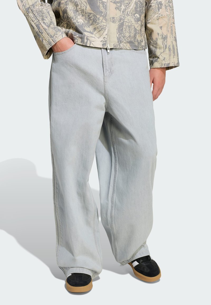 Svetlošedé široké rifle majú mäkkú denimovú textúru, detailné šitie a bočné vrecká, doplnené čiernou obuvou a vzorovanou bundou.