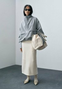 Grå zip-up trøje, cremefarvet nederdel, beige taske. Outfittet har en oversized pasform, glat tekstur og spidse sko med pynt.