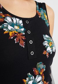 Detailní záběr na černý bezramenný top s květinovým vzorem v tónech tyrkysové, bílé a oranžové a se čtyř tlačítky na hrudi.