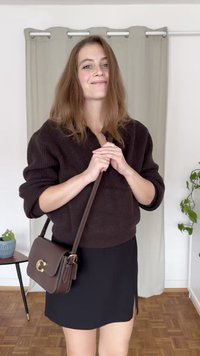 Brauner Strickpullover, schwarzer Minirock mit seitlichem Schlitz und eine kleine braune Umhängetasche mit goldener Hardware. Inneneinstellung mit Pflanzen.