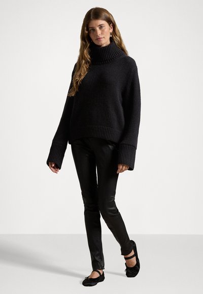 Sort oversized turtleneck sweater med ribbede manchetter og kant, parret med sorte faux læderbukser og sorte flade sko. Glat tekstur.