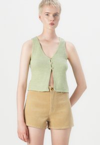 Green ribbed crop tank top with a V-neck and three buttons at the front, paired with beige corduroy shorts. Textured fabric details visible.
