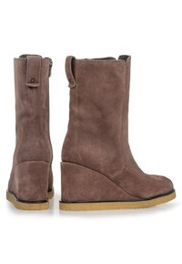 Botas de cuña de ante marrón con una textura suave, punta redondeada y una cremallera en el lado. Con una suela de goma y una altura ligera hasta el tobillo.
