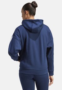 Marineblaue Kapuzenjacke mit lockerer Passform, Kapuze und geripptem Saum. Hergestellt aus einem weichen Material, mit weißen Seitenstreifen und langen Ärmeln.