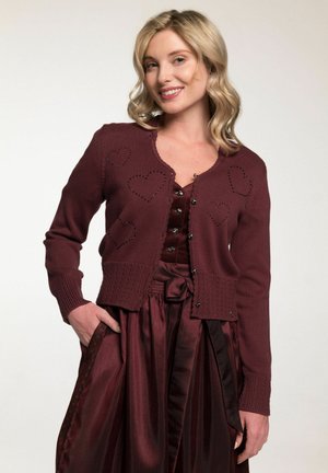Cardigan bordeaux avec des motifs de cœur texturés, des poignets côtelés et une fermeture à boutons. Associé à une jupe en satin assortie avec un détail de taille noué.
