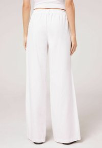 Vita, vida byxor med hög elastisk midja, mjuk textur och rena linjer; inga synliga mönster eller dekorationer.