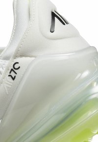 Zapatilla blanca con parte superior de malla texturizada y suela translúcida que presenta un degradado de claro a verde claro. Detalle del logo en negro visible.