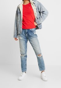Jeansjacka med fårskinnskrage, röd t-shirt, slitna ljusblå jeans och vita sneakers med perforerade detaljer.