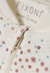 Organic Baumwolljacke mit Reißverschluss, auf einem cremefarbenen Hintergrund mit kleinen rosa und blauen Blumenmustern, weicher Textur und einem Kragen.