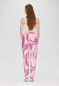 Pantalons en tissu multicolore avec des motifs abstraits rose, crème et violet. Taille élastique et jambes fuselées. Vue arrière présentée.