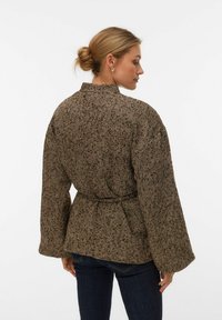 Brūna žakete ar zivju kaula rakstu, josta pie vidukļa un platas piedurknes, ar apkakli un teksturētu audumu.