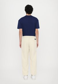Chemise bleu marine à manches courtes associée à un pantalon ample de couleur crème. Le pantalon dispose d'une poche arrière et d'une étiquette de logo. Baskets blanches.