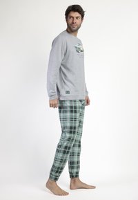 Camisa de manga larga gris con gráfico de coche, combinada con pantalones verdes a cuadros con acentos en blanco y negro. Tejido suave, corte relajado.
