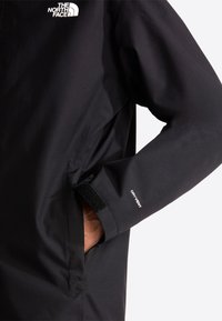 Nærbillede af sort North Face jakkeærme med hånd i lomme, der viser DryVent-logo og justerbar velcrolukning ved manchet.