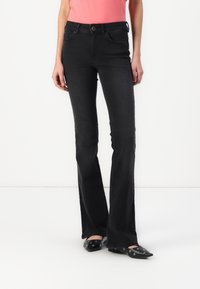 Black flared jeans with a mid-rise waist, featuring front pockets, a button closure, and a clean finish. Worn with black pointed-toe shoes.