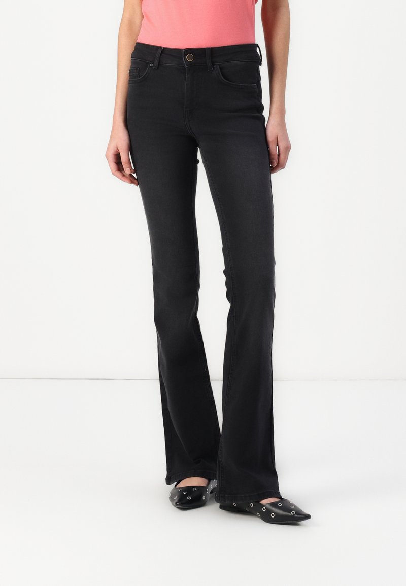 Black flared jeans with a mid-rise waist, featuring front pockets, a button closure, and a clean finish. Worn with black pointed-toe shoes.