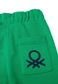 Grüne Baumwoll-Sweatpants mit elastischem Bund, ausgestattet mit einer Gesäßtasche, die mit einem dunkelblauen Logo verziert ist. Glatte Textur, lässiges Design.