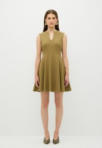 Olivgrünes ärmelloses Kleid mit V-Ausschnitt, schwingendem A-Linien-Rock und glatter Stofftextur. Kombiniert mit passenden grünen Absätzen.
