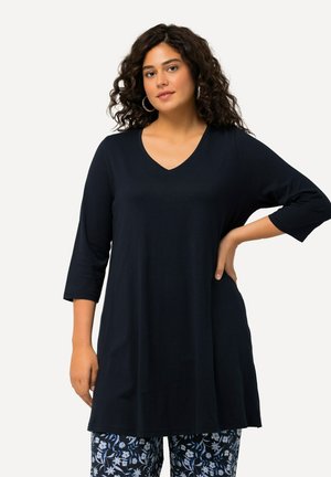 Marineblaue Tunika mit V-Ausschnitt und Dreiviertelärmeln, aus weichem Stoff gefertigt. Kombiniert mit gemusterten, blumenbedruckten Hosen.
