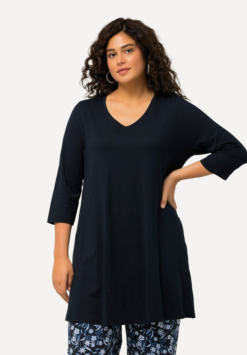 Tummansininen tunika, jossa on V-pääntie ja kolmivartiset hihat, valmistettu pehmeästä kankaasta. Yhdistetty kuvioituihin, kukkakuosisiiin housuihin.