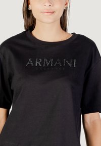 Camiseta negra de manga corta hecha de algodón, con un logo texturizado "ARMANI EXCHANGE" en letras negras brillantes en el pecho.