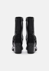 Zwarte leren enkellaarsjes met een ritssluiting, voorzien van een gespsluiting en een chunky hak. Gladde textuur met minimale stikdetails.