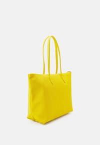 Sac cabas jaune avec deux longues anses, fabriqué en matériau lisse, présentant une forme rectangulaire simple sans pièces métalliques ni ornements visibles.