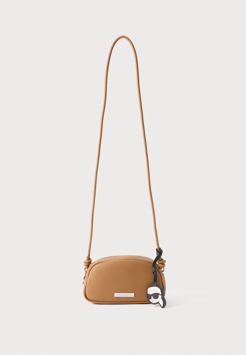 Μικρή ταμπά τσάντα crossbody με μακρύ λουράκι, στρογγυλεμένο σχήμα, υφή στην επιφάνεια και μαύρο μπρελόκ με στυλιζαρισμένο πρόσωπο με γυαλιά ηλίου.