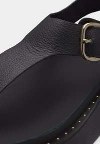 Μαύρο δερμάτινο σανδάλι πλατφόρμα με υφασμένο λουράκι, χρυσή αγκράφα, λείο πέλμα και μικρές χρυσές καρφίτσες κατά μήκος της ακμής της σόλας.