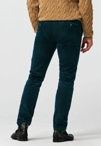 Donkergroene corduroybroek met een strakke pasvorm, met een taille op middenhoogte, achterzakken en een subtiele verticale textuur, gecombineerd met zwarte laarzen.