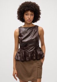 Hnedý peplum top s textúrovaným saténovým povrchom, lodičkovým výstrihom a bezrukávovým dizajnom. Skombinovaný s krátkou sukňou s houndstooth vzorom.