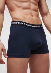 Tengeri kék pamut boxeralsó, fekete derékrésszel, amelyen fehér "KARL LAGERFELD" logó található, testhez simuló kialakítással és rövid szárhosszal.