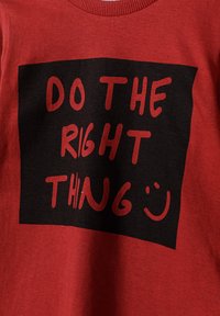 Rød bomulds T-shirt med en iøjnefaldende sort firkant med teksten "GØR DET RETTE" i rød, og et smilende ansigt som accent. Blød tekstur.