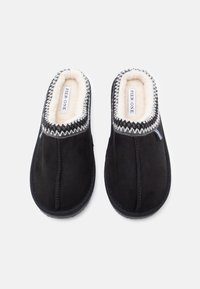 Crne zamšaste papuče s plišastom bijelom podstavom, zaobljenog oblika, ukrasnim sivim šavovima i debelim gumenim đonom. Brand oznaka vidljiva unutar.