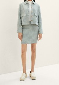 Giacca in tweed azzurro chiaro con due tasche frontali, abbinata a una gonna coordinata. Sotto, un dolcevita bianco e scarpe mocassino beige completano l'outfit.