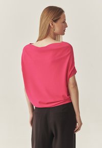 Lös passande, klarrosa topp med bred rundringning, korta ärmar och slät textur, bärs med mörka, strukturerade byxor.