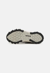 Semelle extérieure de chaussure de trail running, présentant une texture en caoutchouc noir avec des motifs hexagonaux et une semelle intermédiaire beige pour une meilleure traction et durabilité.