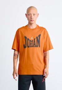 Orange bomulds t-shirt med stort sort "JORDAN" print. Korte ærmer, rund hals og løs pasform. Minimalistisk design med logo detaljer.