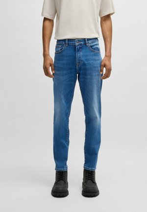 Jeans de mezclilla azul con un corte ajustado, que presentan un ligero desgaste, cinco bolsillos y cierre de botón, combinados con botas negras con cordones.
