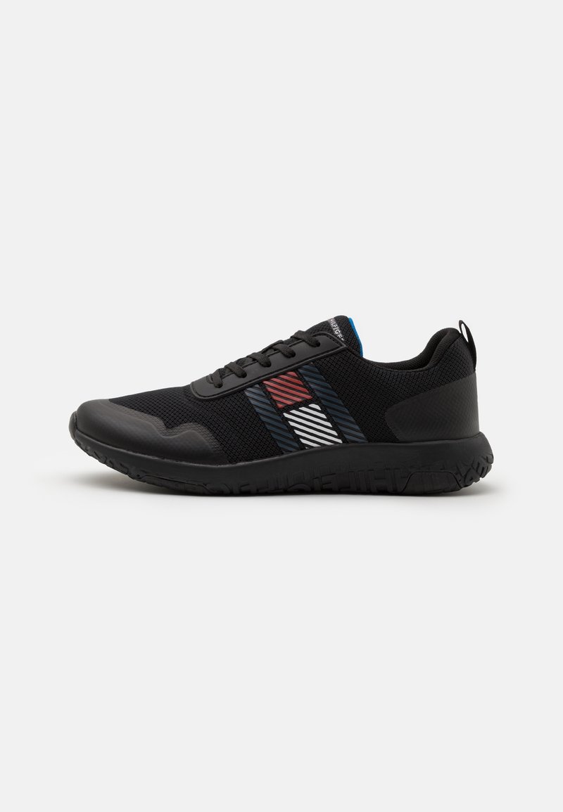 Baskets en mesh noir avec semelle noire, motif latéral rayé rouge, blanc et bleu, et lacets noirs sur fond neutre.