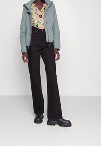 Veste bleu clair avec capuche, chemise à fleurs rose et verte, pantalon noir droit et bottes noires épaisses. Textures lisses partout.