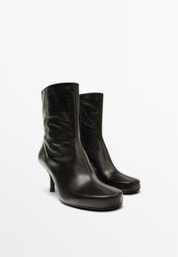 Stivali neri in pelle fino alla caviglia con punte affusolate, una finitura lucida e un tacco a stiletto di altezza media. Cuciture decorative lungo la parte anteriore.