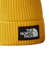 Yellow knitted beanie with a ribbed texture and a black rectangular patch displaying "THE NORTH FACE" in white lettering.